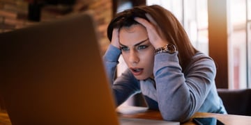 Woman with hands over head looking at PC screen