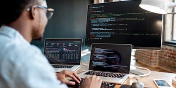 Coder in front of three computers with code on screens