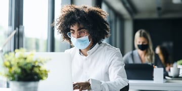Person with mask sitting in front of PC