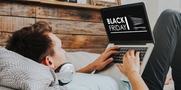 Young man laying on bed and looking at laptop screen with Black Friday