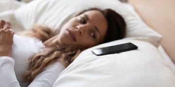 Woman laying on bed and looking anxiously at mobile nearby