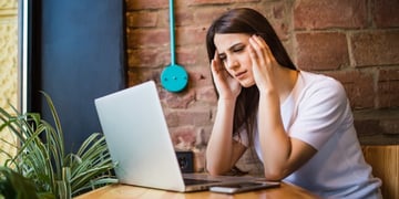 Concerned woman holding hands on head and looking at PC