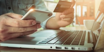 Man holding mobile and credit card above laptop