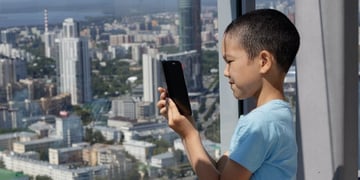 A Muslim boy uses a smarphone against the background of a panoramic window. Blurred view of the city