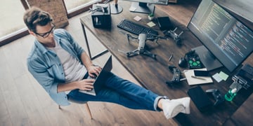 High angle view of a focused man typing laptop with legs on table