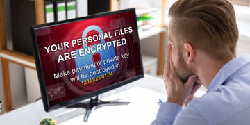 Worried Businessman Looking At Computer With Ransomware Word On The Screen At The Workplace