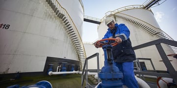 man working with large white fuel containers against blue sky