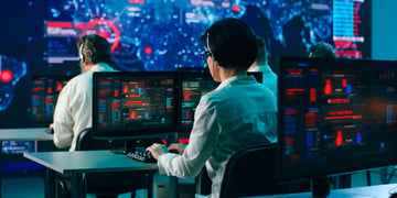 Rack focus of anonymous men and woman sitting at desk and writing security codes on computers during