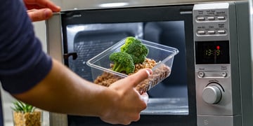 Using the microwave oven to heat food. Woman's hand puts plastic container with broccoli and buckwhe