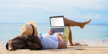 Man reading email on laptop while relaxing on beach