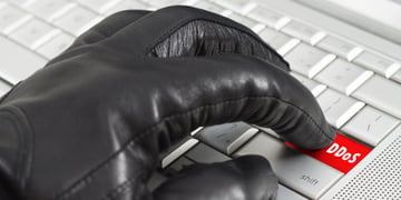 Gloved hand clicking DDoS button on keyboard