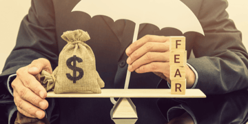 Businessman's torso with wooden scales balancing moneybag and word fear