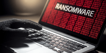 Hand with black glove typing on red matrix laptop screen with Ransomware inscription
