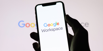 Shadowy hand holding mobile phone with Google Workspace logo on it