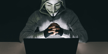 Anonymous masked guy in front of laptop folding hands