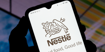 Shadowy hand holding mobile phone with Nestle logo displayed