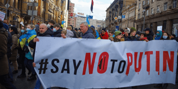 Crowd demonstrating in a city with a banner saying #SayNoToPutin