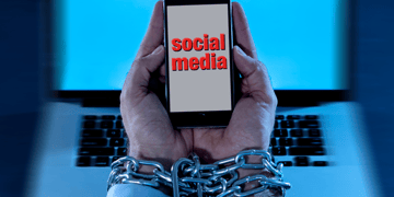 Chained hands struggle to use social media on mobile phone, with computer in background