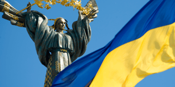 Ukrainian flag flying on sunny day with independence monument in background