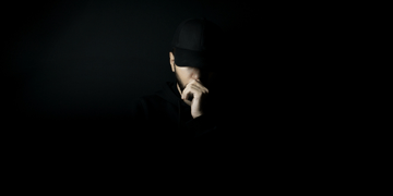 Young man in a black baseball cap, so deep in shadow you can only see part of his face.
