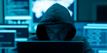 Asian man looking intently at a laptop, face partly concealed