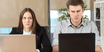 Two annoyed workers glaring at each over their laptops
