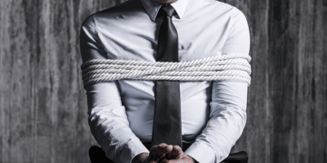 Man in suit and tie, tied to a chair. No head shot.