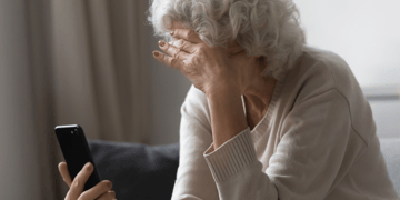 Elderly woman holds head in one hand and mobile in the other