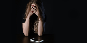 Woman holding head in hands with cellphone