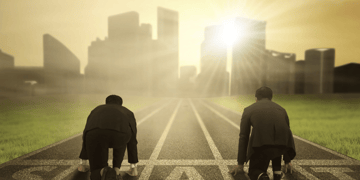 Two men in business dress kneeling on a race track towards a bright cityscape - but who wins?