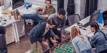multiethnic colleagues playing in table soccer at modern office