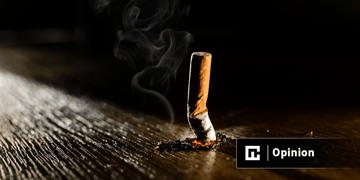A smoking burning cigarette on a dark floor background.