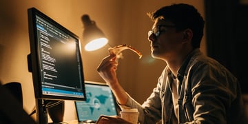 young programmer at home working and eating pizza