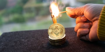 Hand holding lit matches to cryptocurrency coins