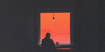 Remote work; the silhouette of a person sitting in front of a window, a shadow in a warm red light