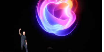 Apple CEO Tim Cook on black stage with two fingers up, glowing apple logo