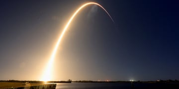 Rocket launches, leaves a yellow light trail in violet sky above water