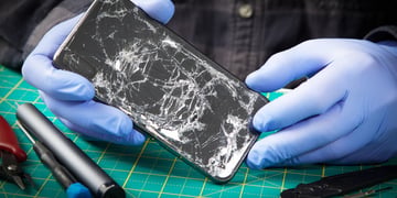 black smartphone with smashed screen held by hands in blue rubber gloves