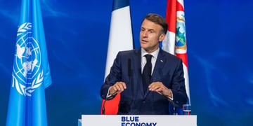 Emmanuel macron on podium with UN and France flag, blue background