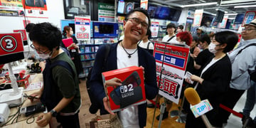 asian map smiling widely with eyes closed, holding nintendto switch 2 black box