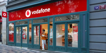 vodafone store with logo, asian woman walking out through the door in white throusers and orange top