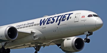 white plane in a blue sky, blue WestJet sign, canada flag