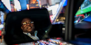 An uber driver, in the city, seeing himself in the wing-mirror.