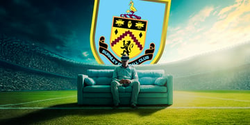 man sitting on a light blue sofa n the middle of a football stadium, crowd, green grass