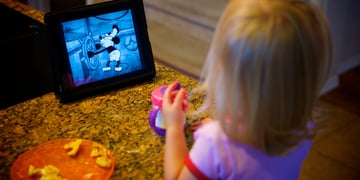 A small girl watching mickey mouse on her ipad.