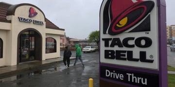 A taco bell drive thru sign and some customers approaching the restaurant