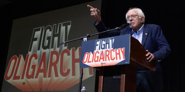 Bernie Sanders speaking on the podium among slogans reading "Fight Oligarchy"