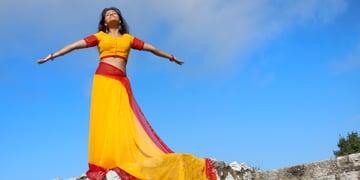 young indian woman standing on rock wall, yeallow red sari