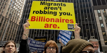 A person holding a sign that reads migrants aren't robbing you billionaires are