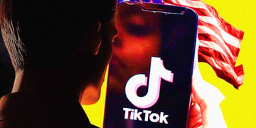 A person looks at a smartphone with a TikTok's logo on the screen, the US flag behind it